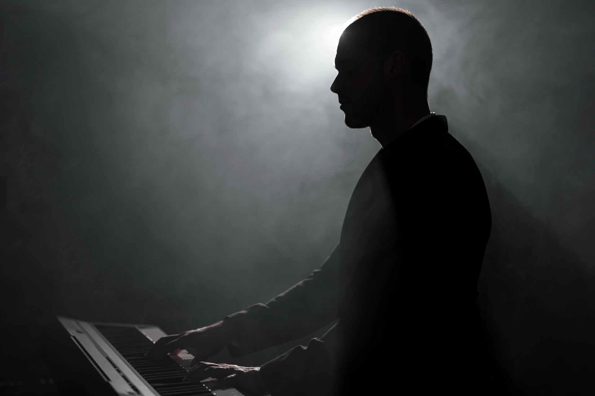 Pianist i silhuett spelar piano i ett mörkt rum fyllt av rök