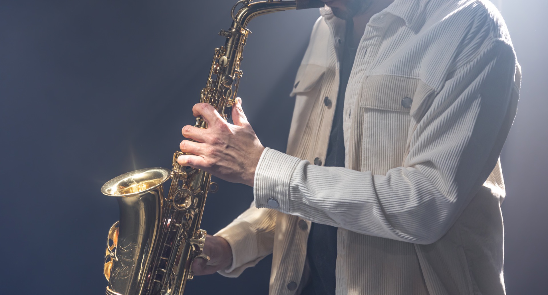 Saxofonist i vit skjorta spelar altsaxofon på en mörk scen med rök