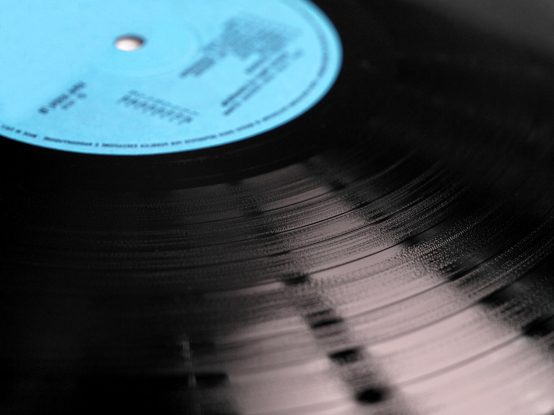 Svart vinylskiva i närbild med ljusblå etikett och glänsande spår