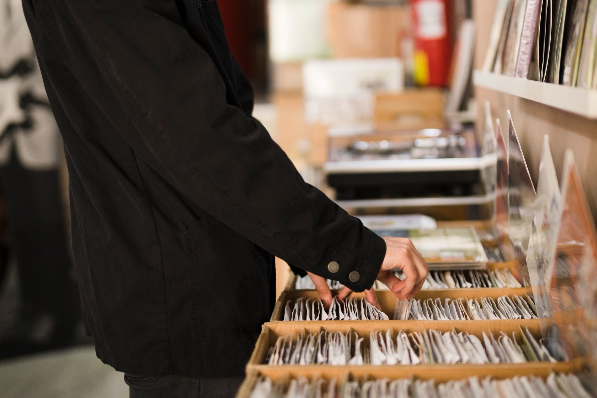 En hand bläddrar bland vinylskivor i en back i en skivaffär