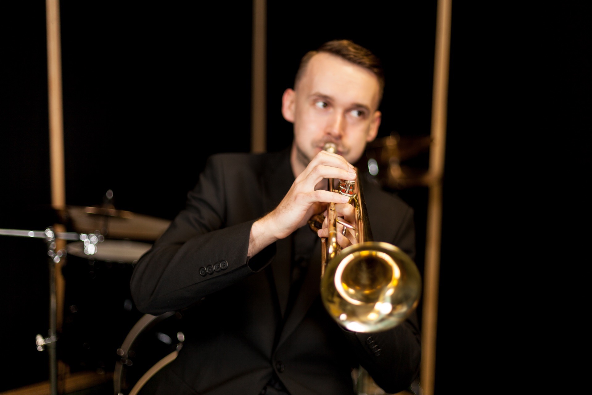 Trumpetare i mörk kavaj spelar framför ett trumset på en mörk scen